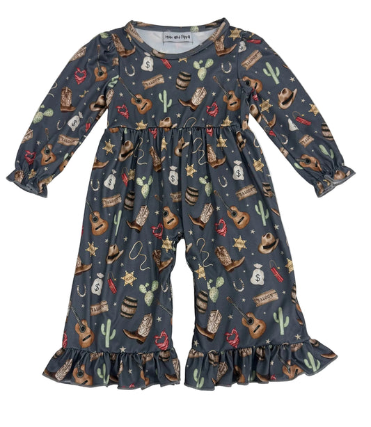 A toddler's long-sleeve jumpsuit with a western-themed print, featuring cowboy boots, cacti, stars, and horseshoes on a dark slate gray background. The jumpsuit has ruffled cuffs and a ruffled hem, and is laid flat on a white background.